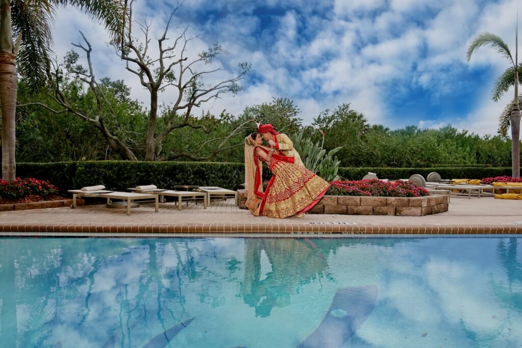 woman in pink dress sitting on brown wooden bench near swimming pool during daytime- destination wedding India